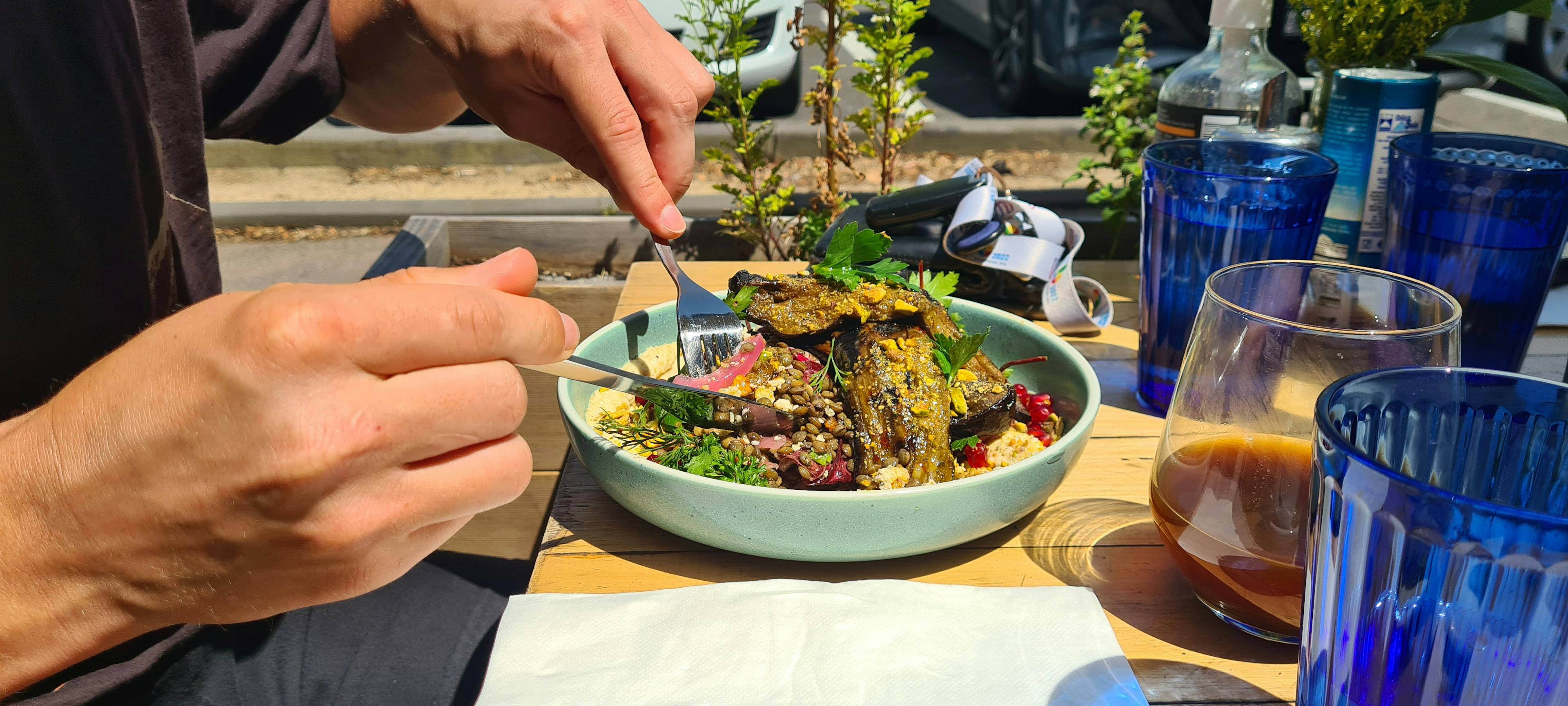 Roasted eggplant on a bed of grains with two hands holding a knife and fork