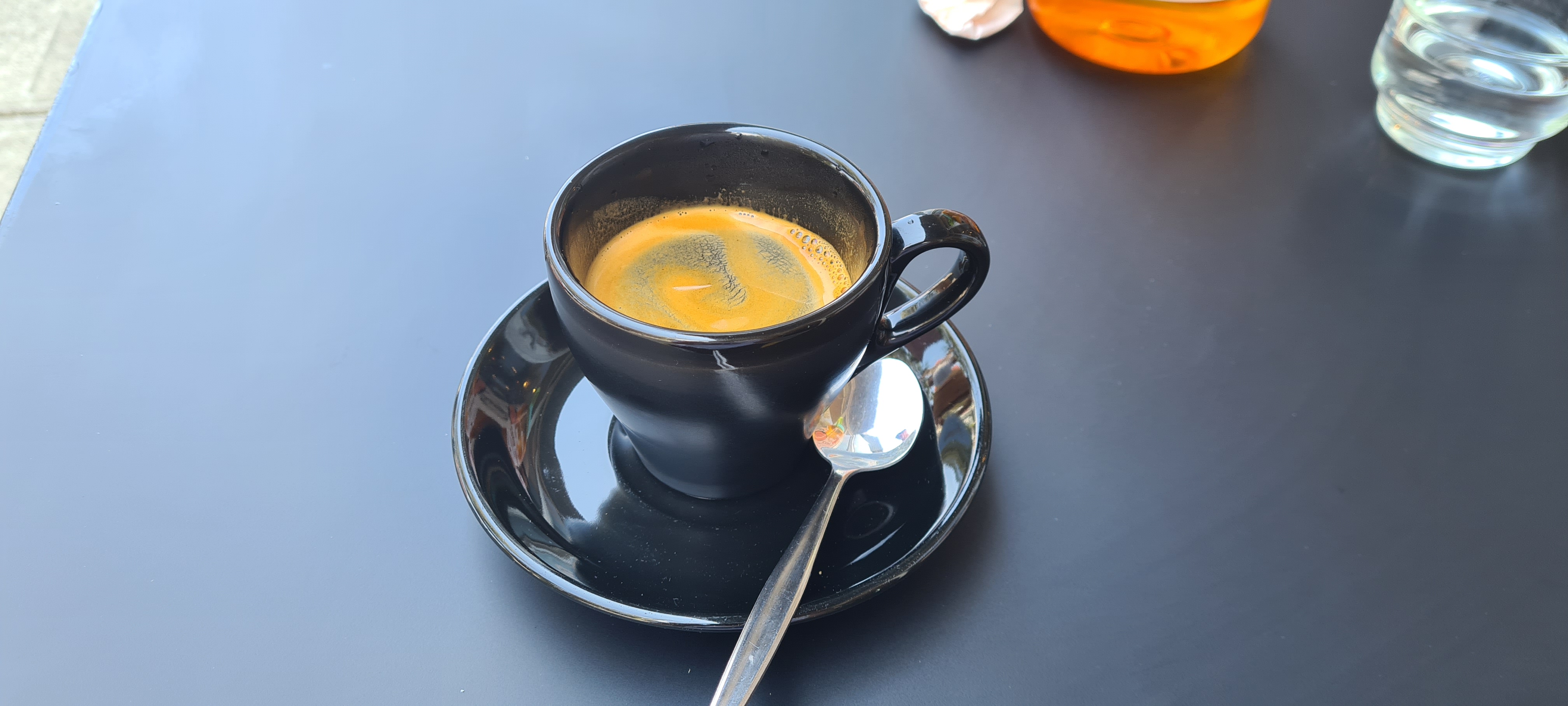 Small long black coffee with a contrasting swirled crema in a black mug 