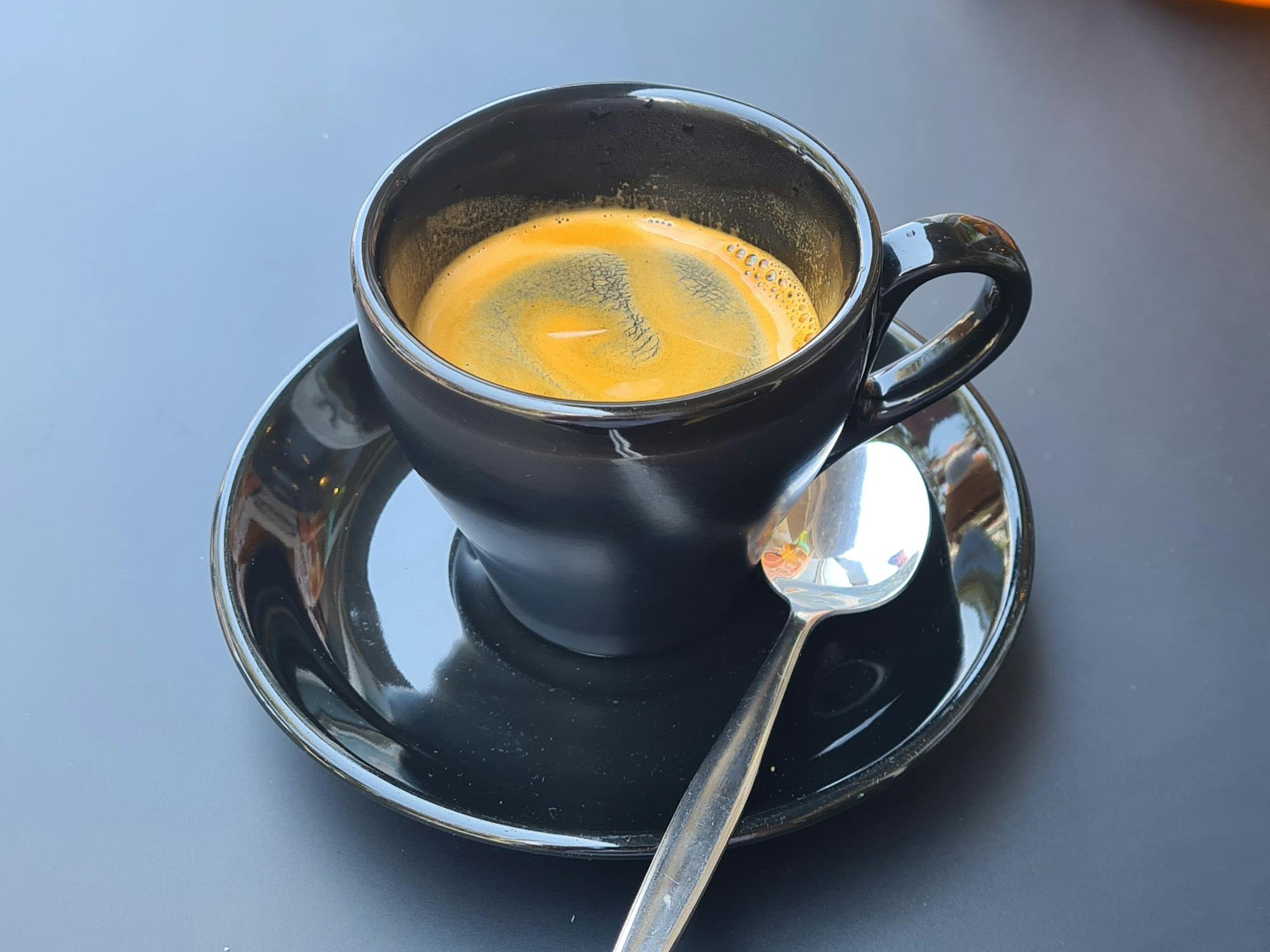 Small long black coffee with a contrasting swirled crema in a black mug 