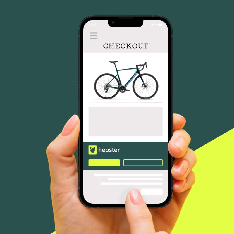 Hand is holding a smartphone that shows a mock up of checkout and a picture of a bike