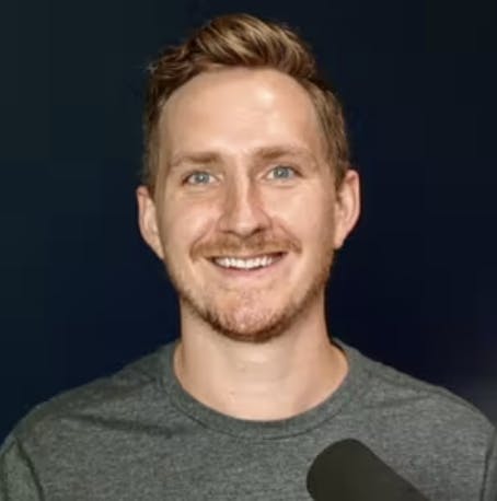 Headshot of Alban Brooke in front of a mic with a black background behind him