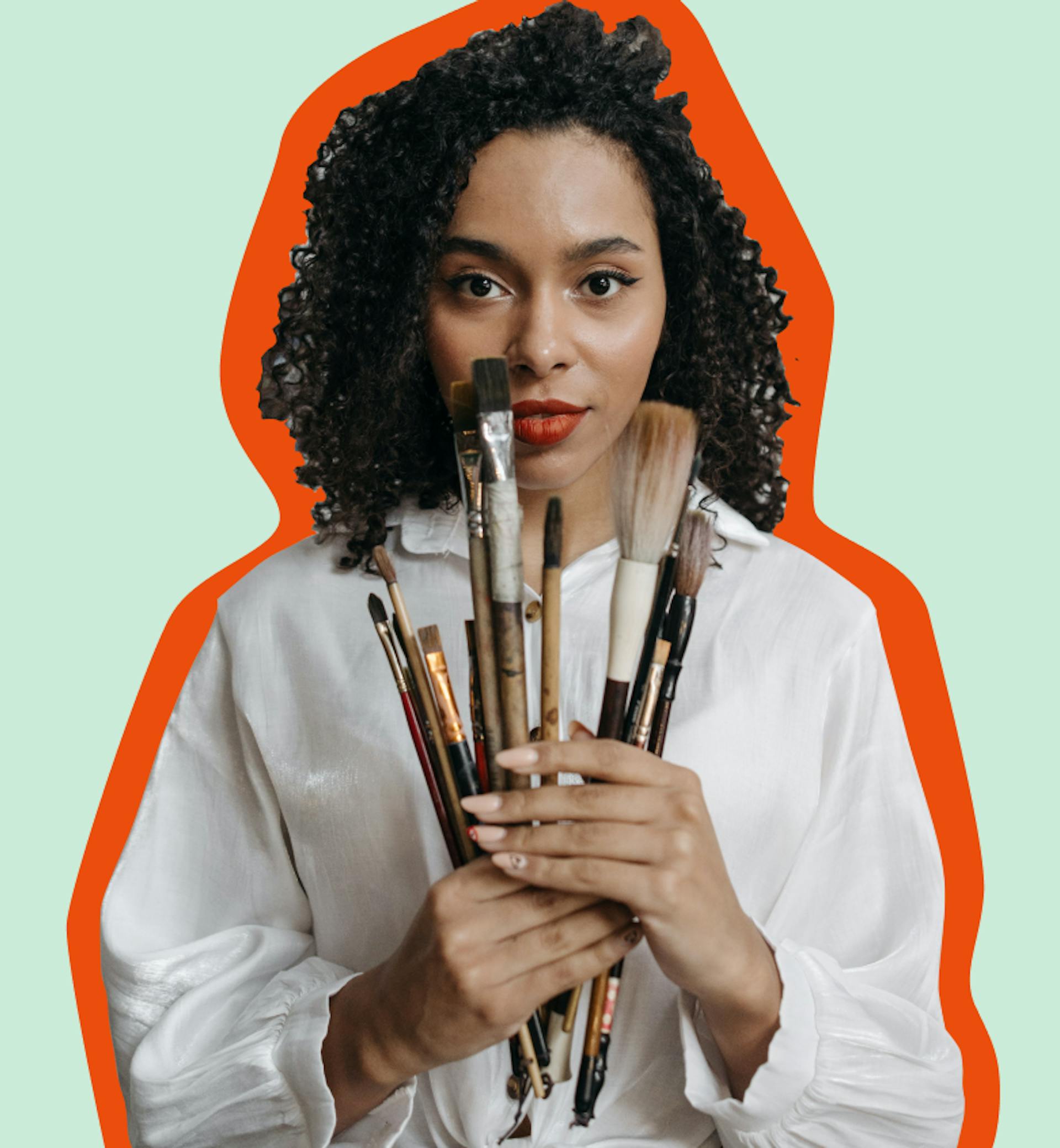 Girl with paint brushes fanned out in front of her looking directly into the camera