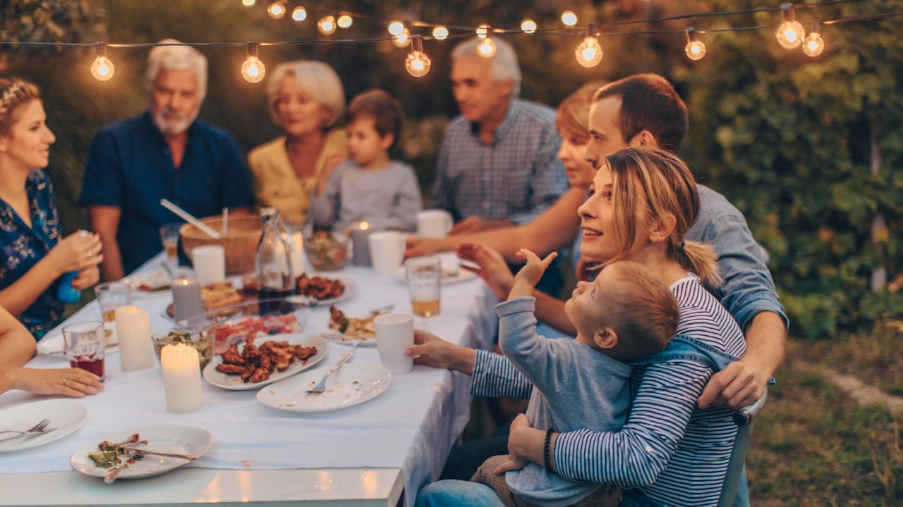 Large multi-generational family eating dinner outside under lights