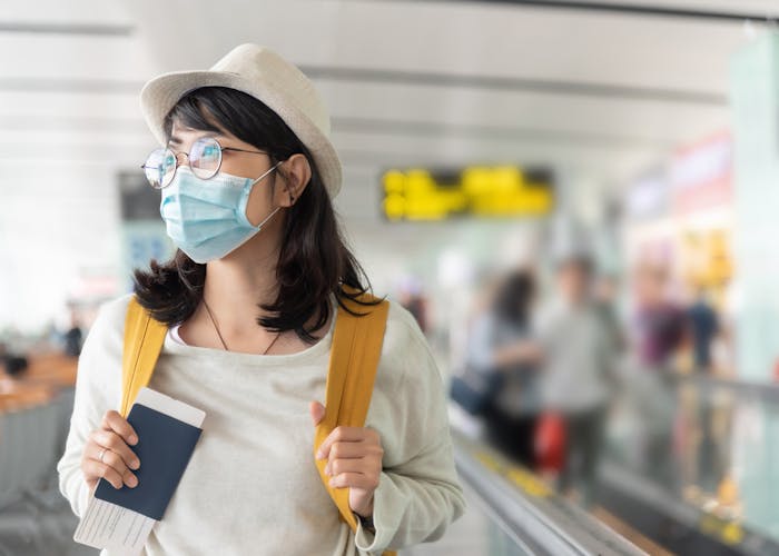 Woman holding passport in the airport wearing a mask