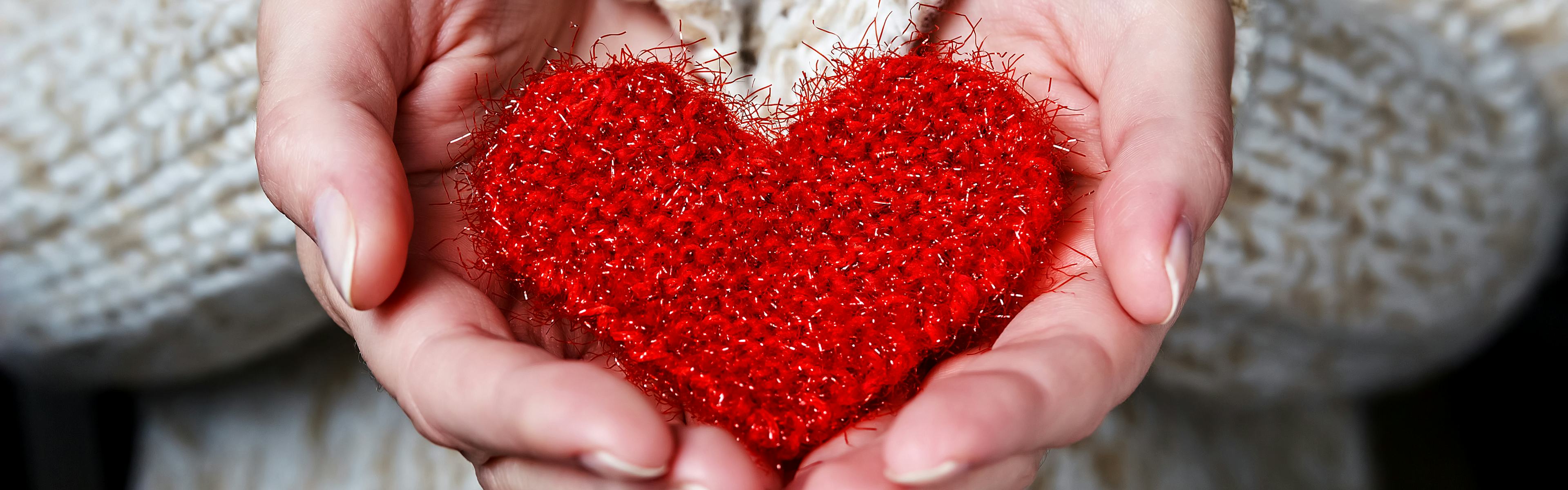 Woman's hands holding a red knitted heart
