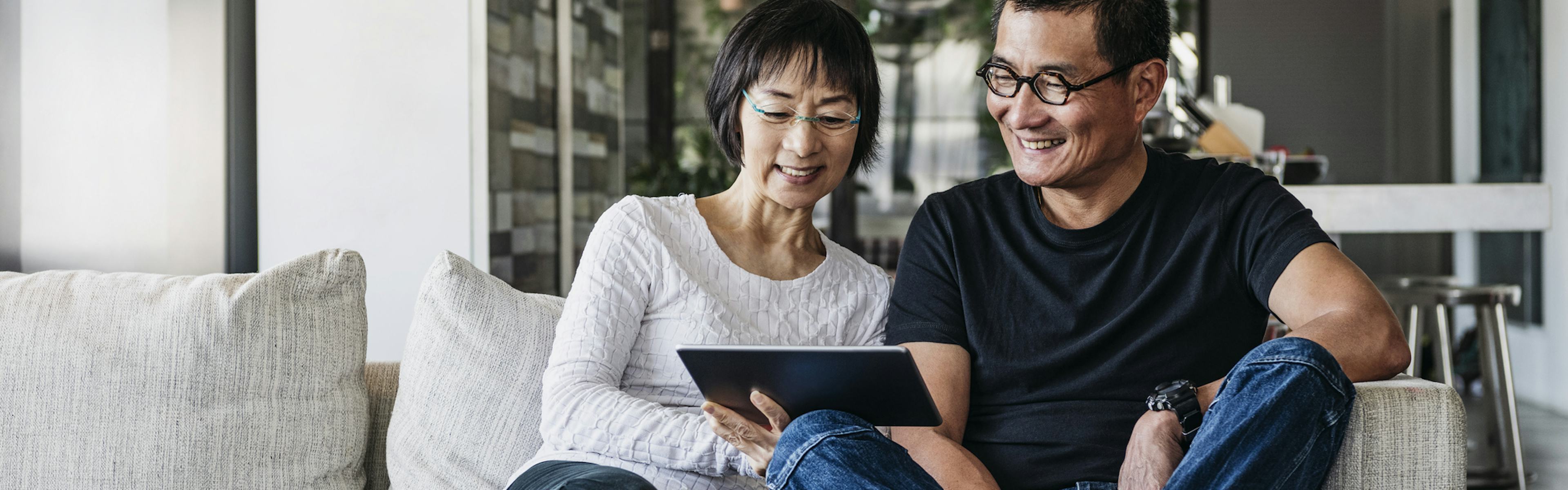 Middle aged couple sitting on couch, smiling looking at a tablet