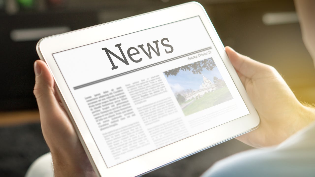 A man holding a tablet displaying news