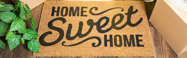 Image of a door mat saying Home Sweet Home surrounded by moving boxes