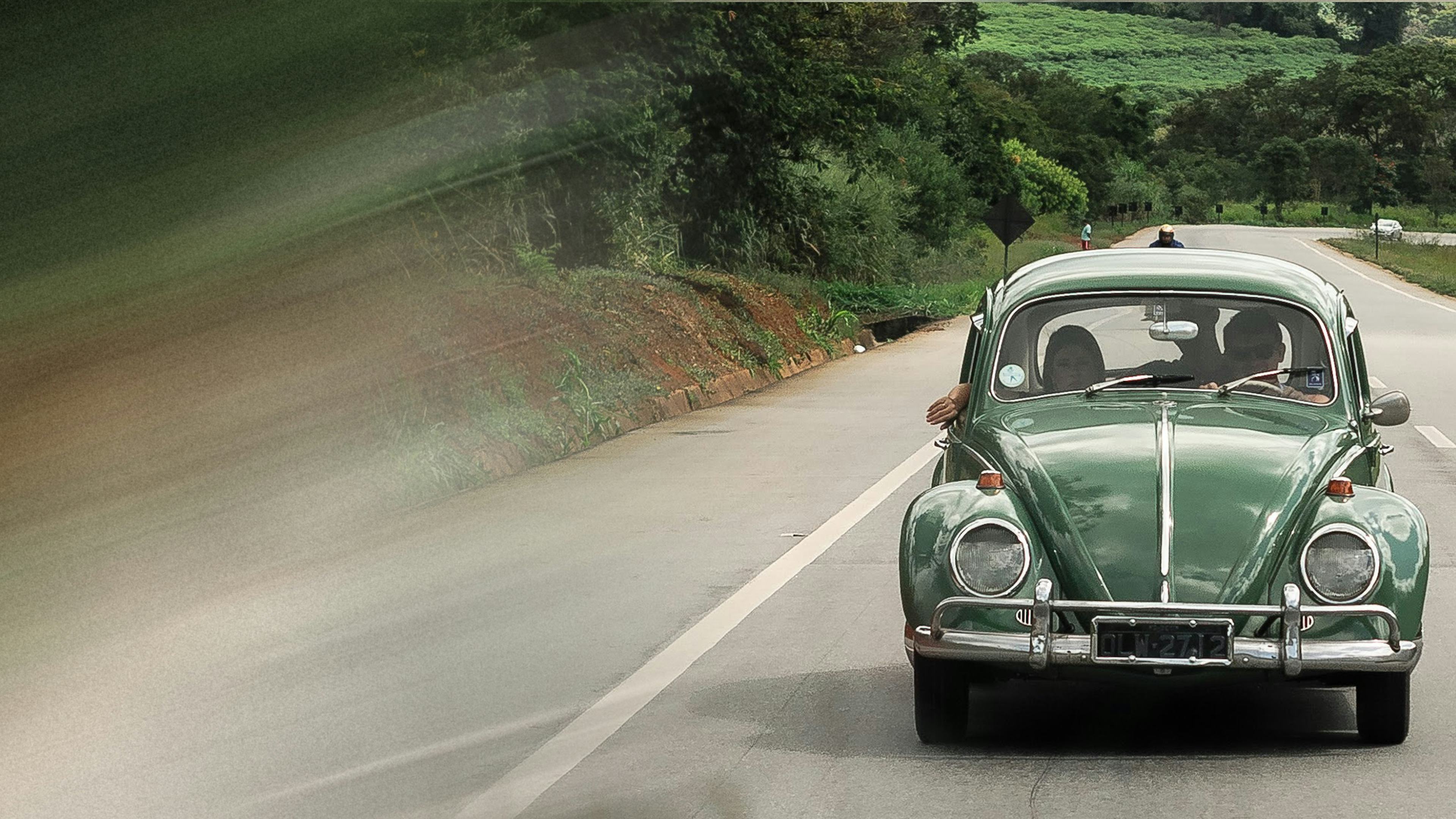 Couple in classic green Volkswagen car driving down a highway with forest in background. Get CAA roadside assistance today for more comprehensive coverage than your manufacturers roadside assistance plan (including honda roadside assistance, hyundai roadside assistance, ford roadside assistance, mazda roadside assistance, nissan roadside assistance)