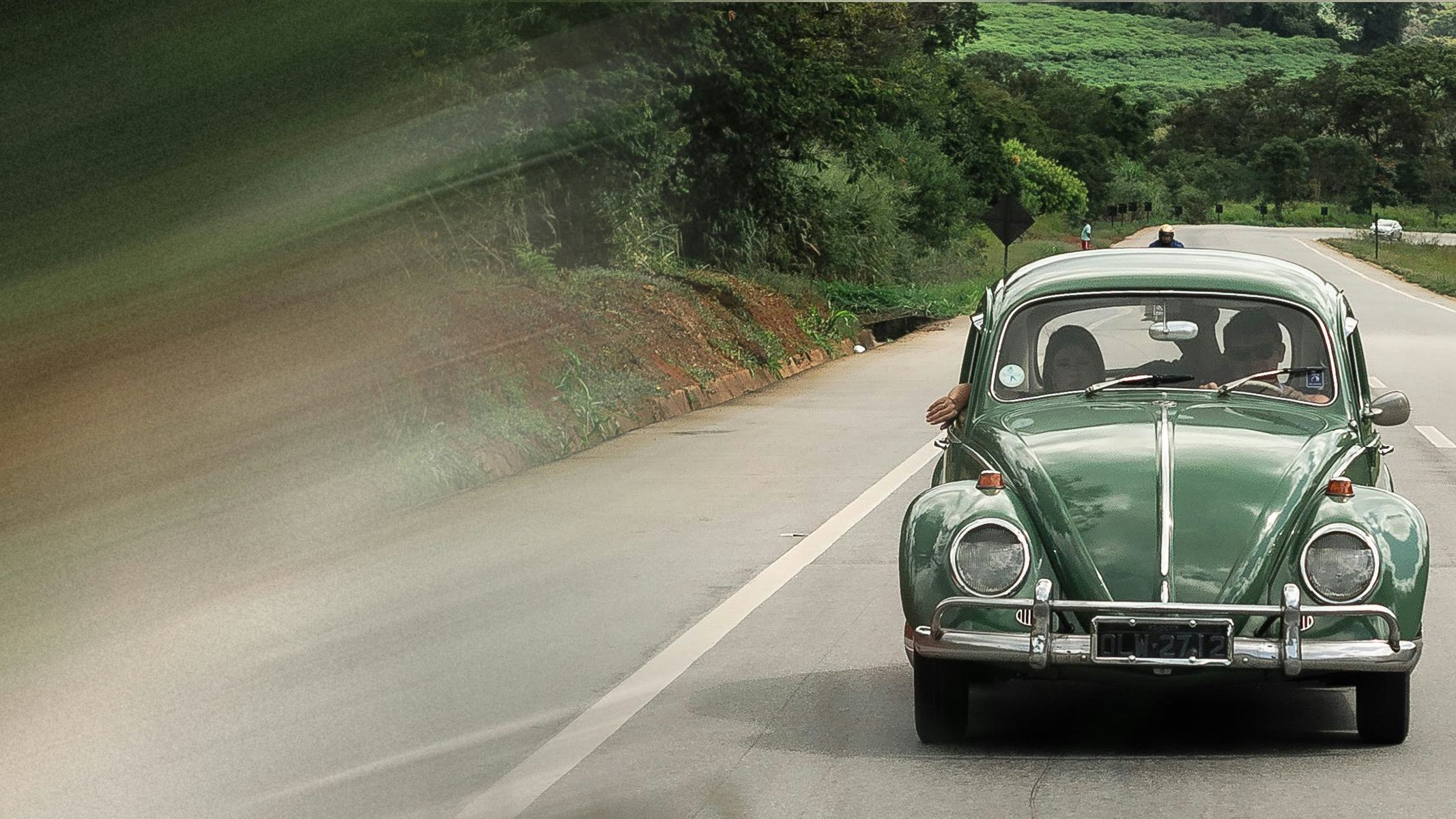 Couple in classic green Volkswagen car driving down a highway with forest in background. Get CAA roadside assistance today for more comprehensive coverage than your manufacturers roadside assistance plan (including honda roadside assistance, hyundai roadside assistance, ford roadside assistance, mazda roadside assistance, nissan roadside assistance)