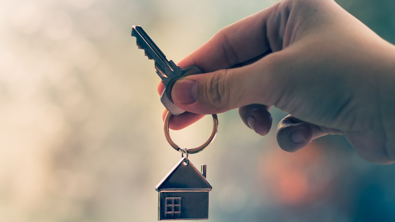 A person is holding a key in their hand with a keychain shaped like a house.