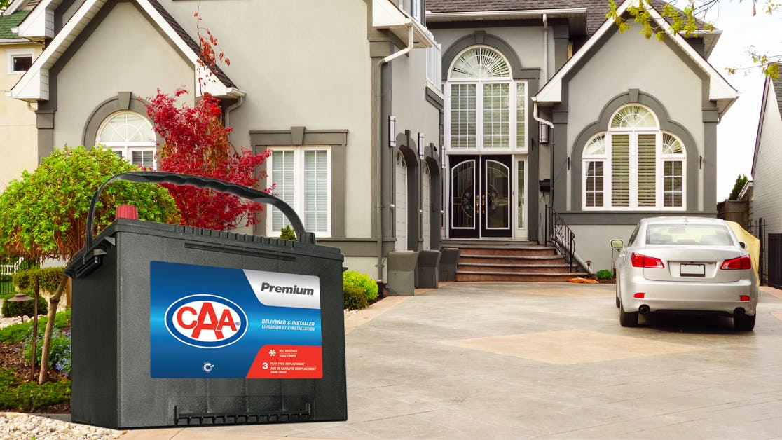 CAA Premium battery in front of a house with a car parked in the driveway.