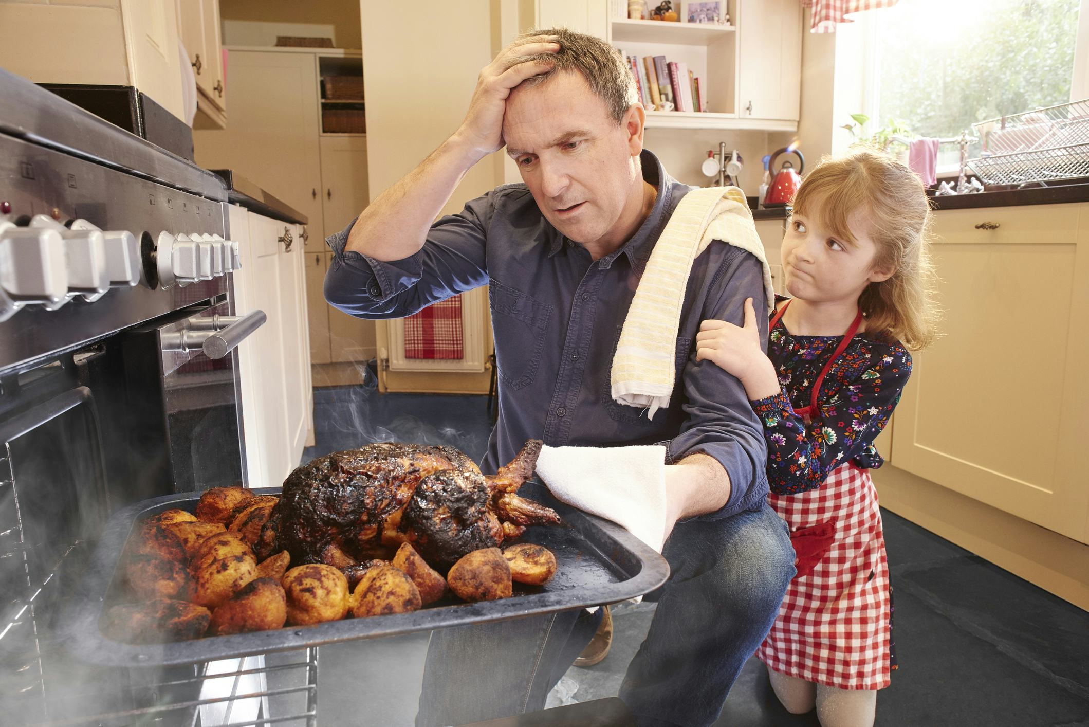 A father pulls a burnt turkey out of the oven and his little daughter consoles him.