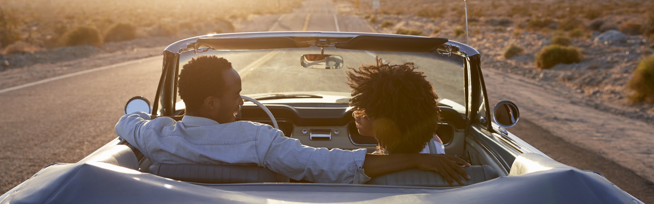 Rear view of couple on road trip in convertible at sunset
