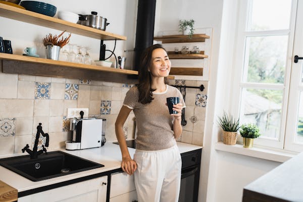 A lady standing in her kitchen drinking from a mug.