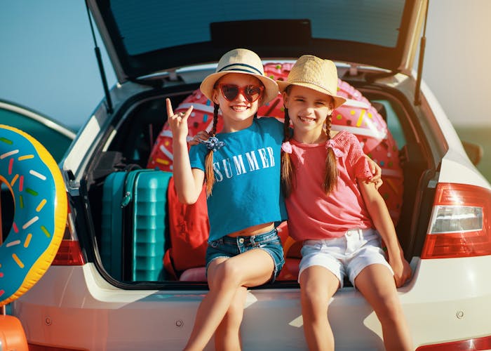 Two kids stting in open trunk of station wagon ready to go on a summer road trip