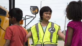 a child wearing a CAA vest helping kids onto a school bus