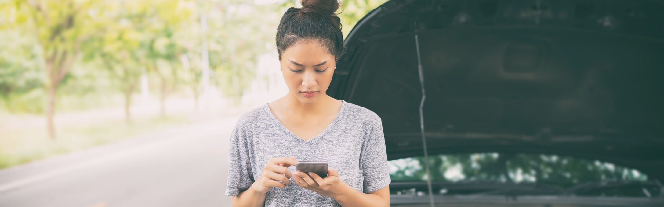 Asian woman using mobile phone to request roadside assistance