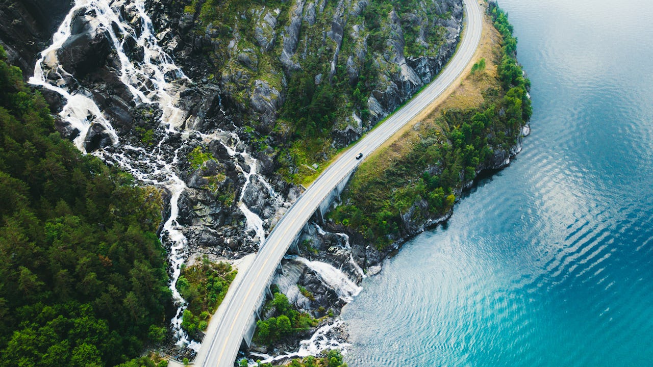 Scenic mountain road with car, sea and waterfall in Norway