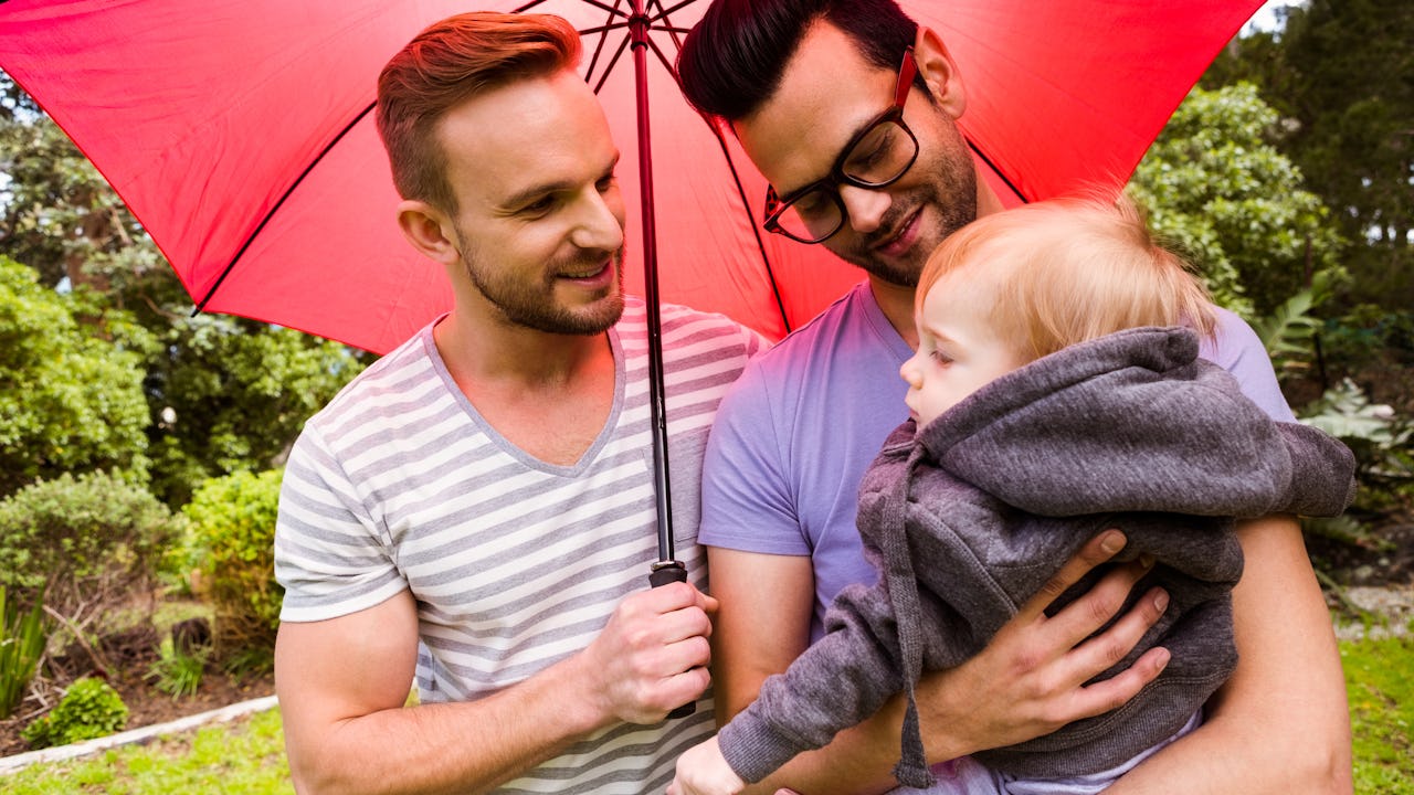 Same sex couple with young child under an umbrella