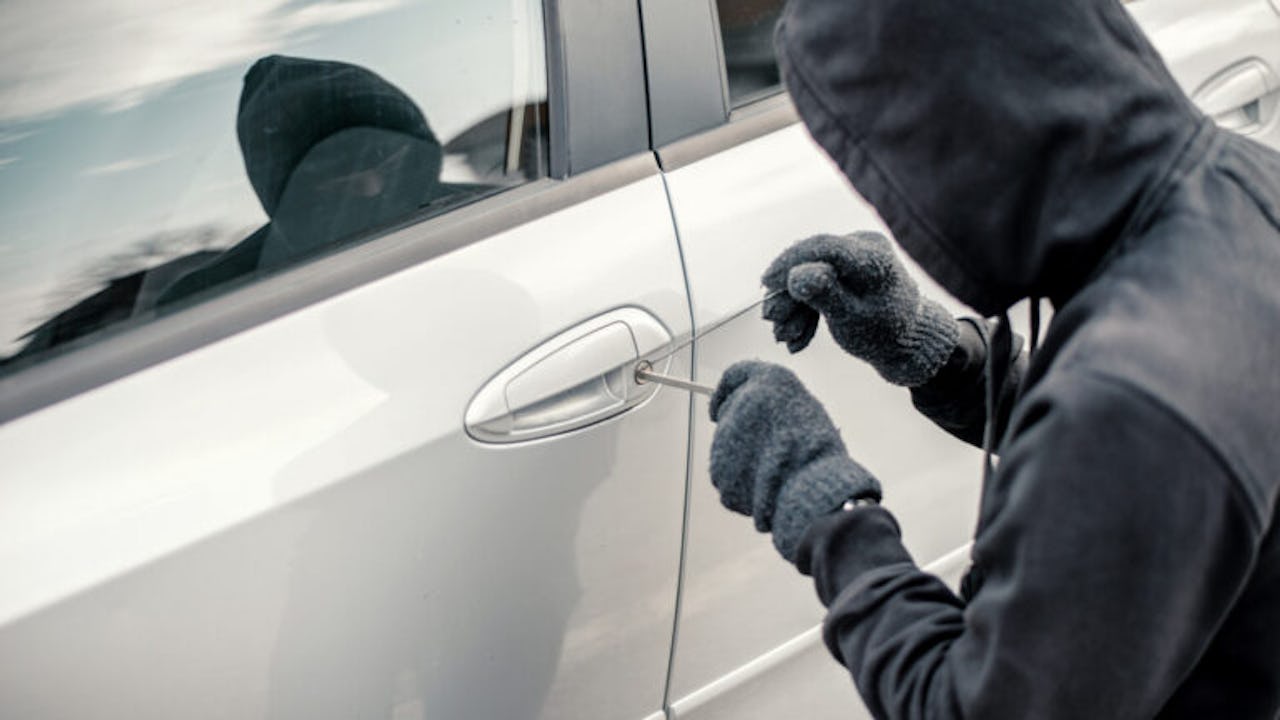 A hooded thief picking the lock of a car