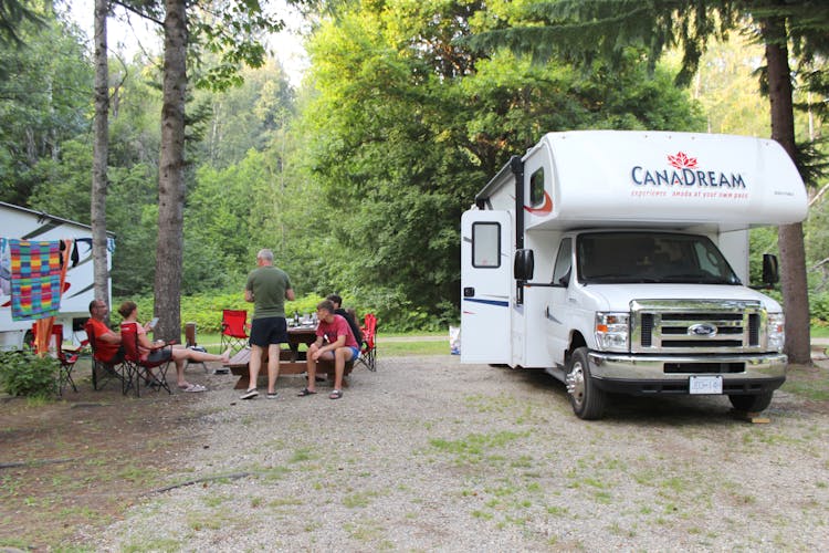 CanaDream RV parked at a campsite with family sitting outside