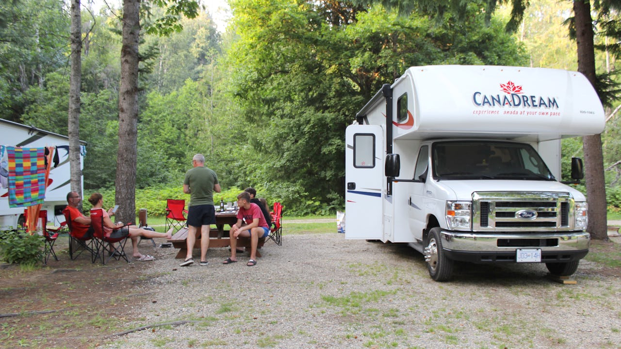 CanaDream RV parked at a campsite with family sitting outside