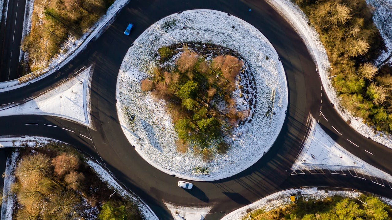 A roundabout with a few vehicles on the road and snow on the ground