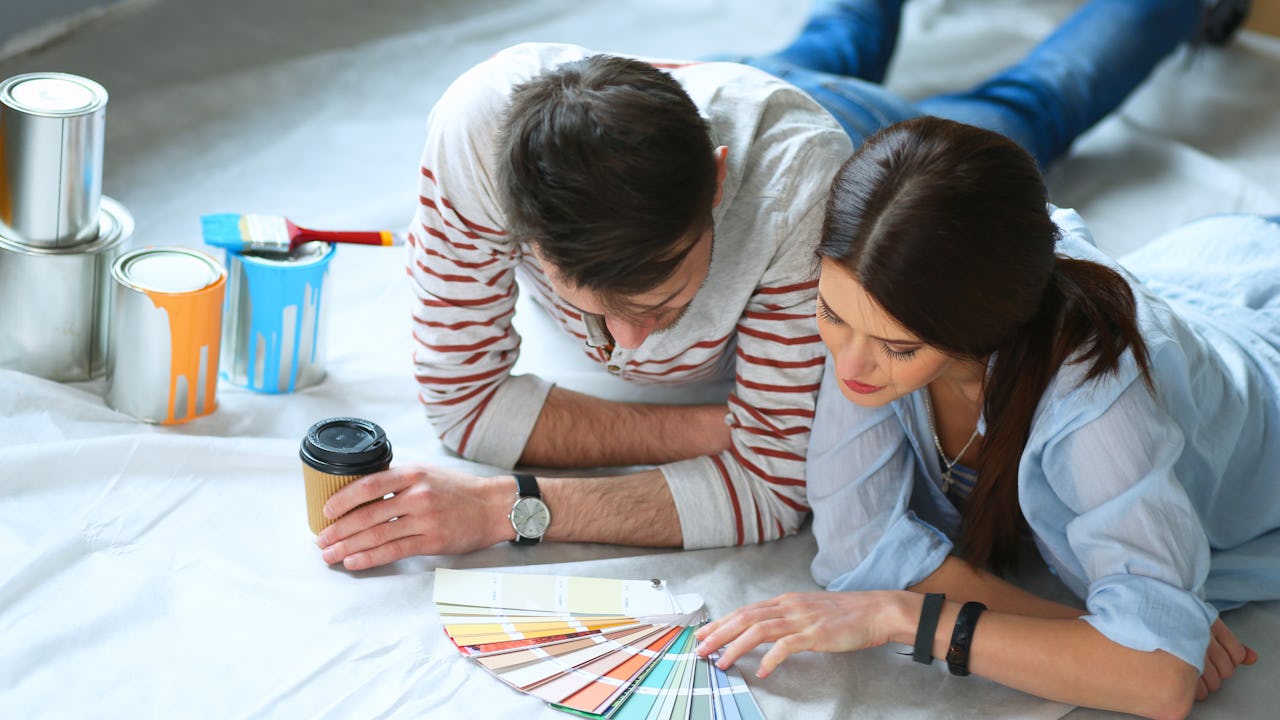 A man and woman laying on the floor looking at paint colour chips