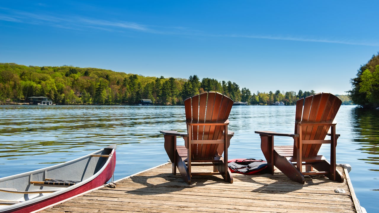 Dock with 2 adirondack chairs on it with a canoe in the lake