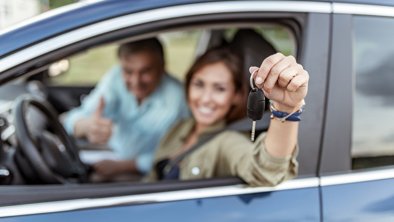 A young woman in a car is happily holding up her car key.