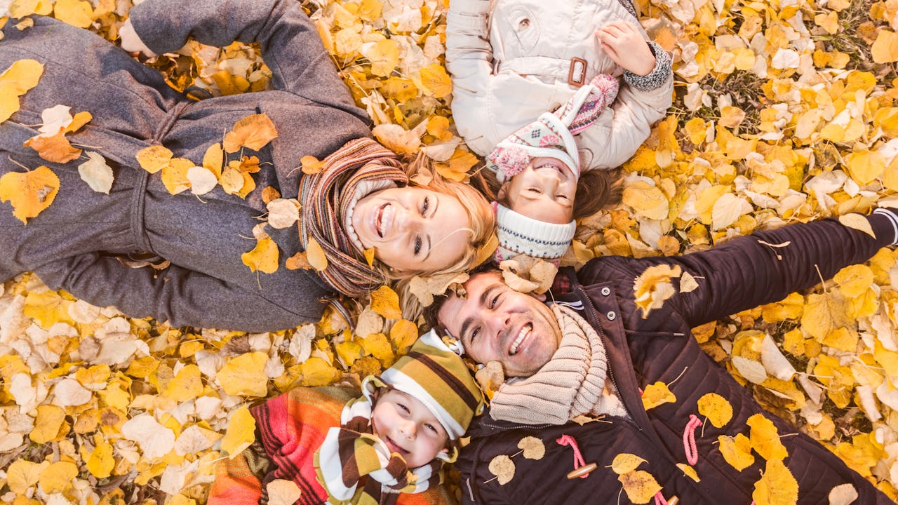 High angle view of happy parents having fun with their children, lying down in heap of leaves and looking at camera.