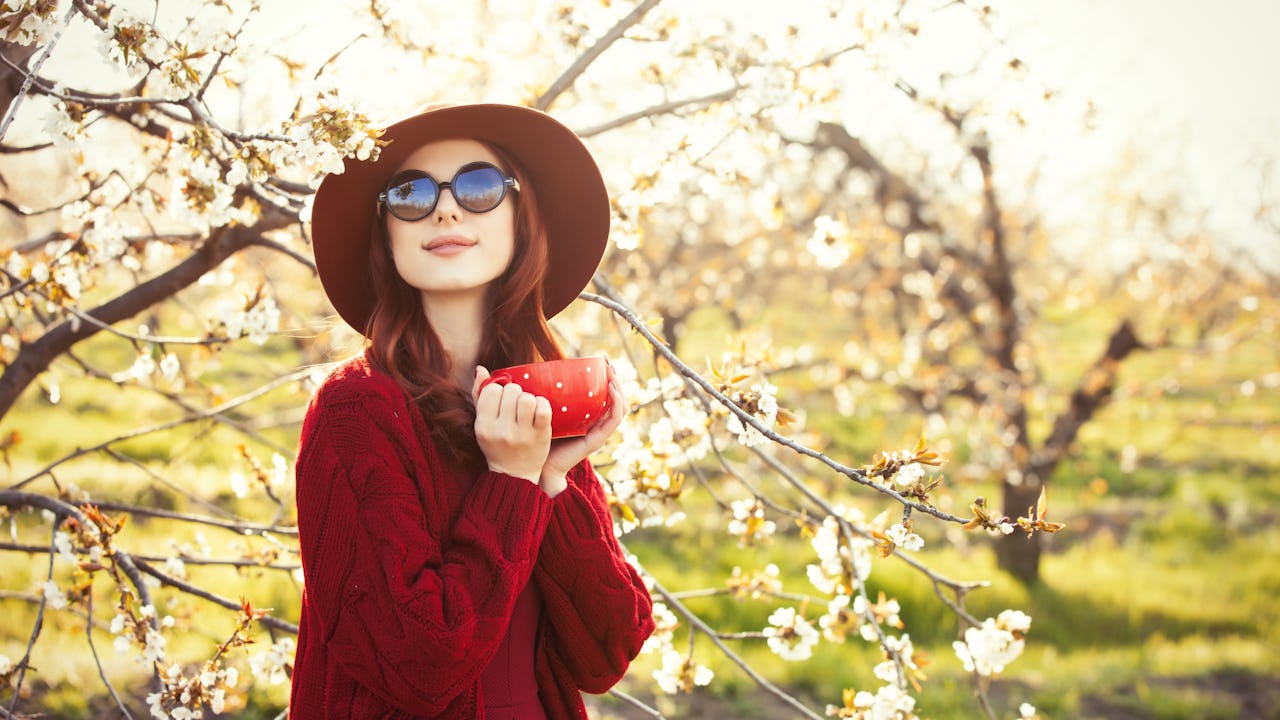 A young woman in sunglasses enjoying a cup of coffee outdoors