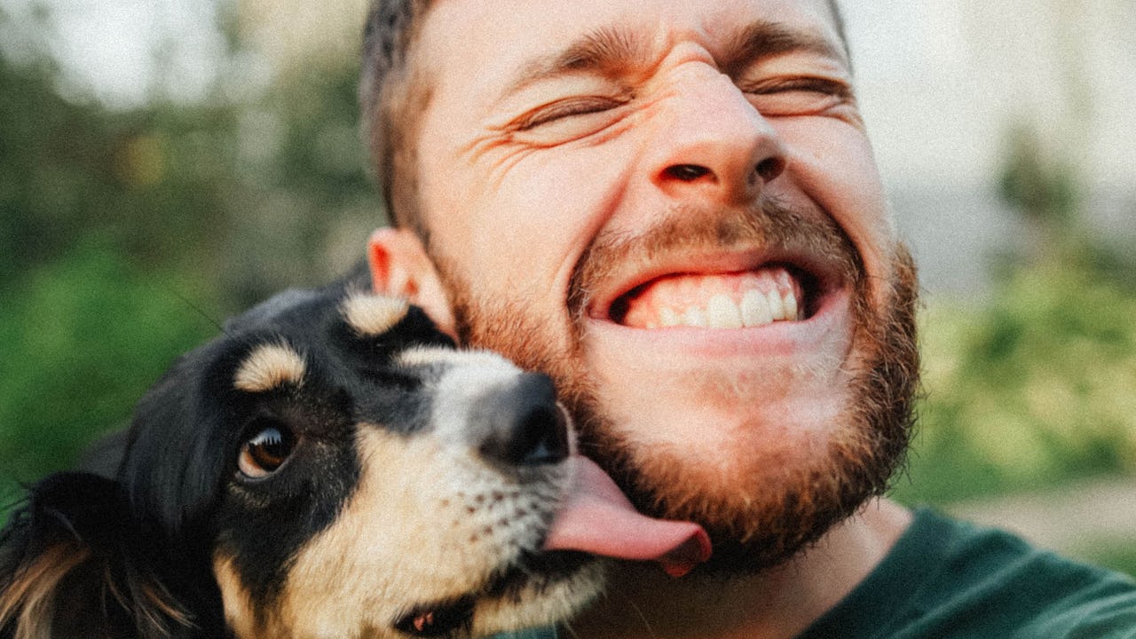Man holding his dog and smiles as the dog licks his face