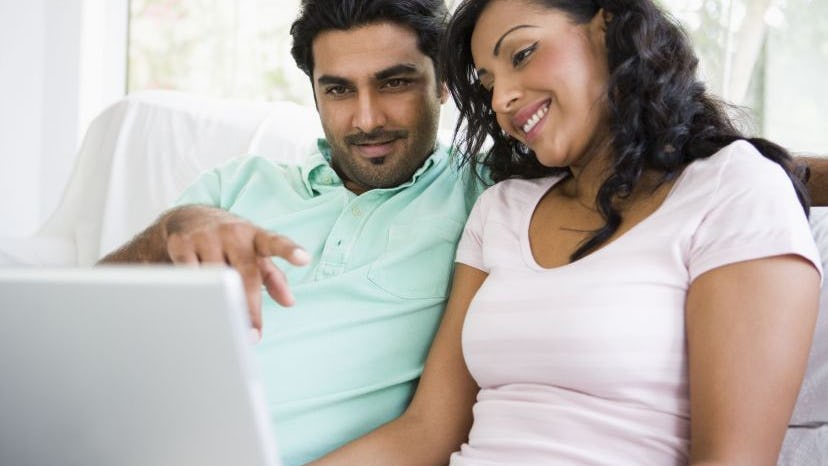 A couple sitting on a couch looking at a laptop
