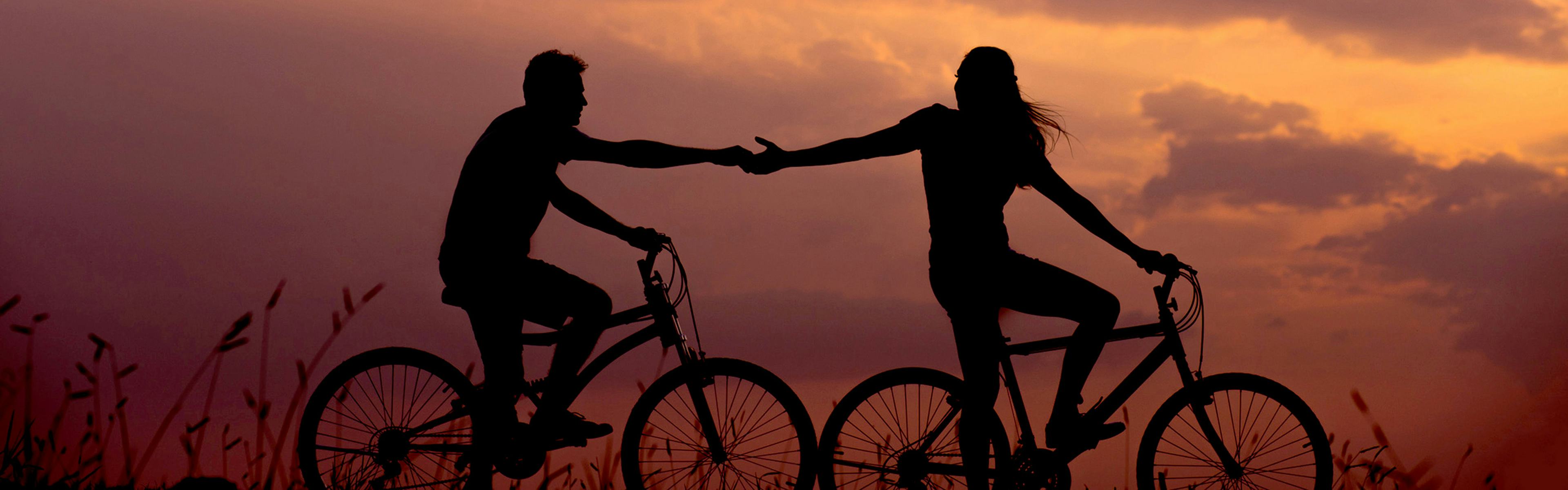 A couple rides bicycles at sunset.