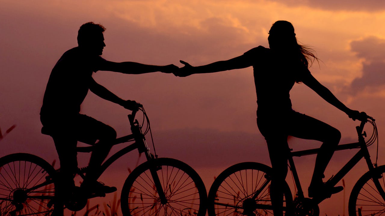 A couple rides bicycles at sunset.