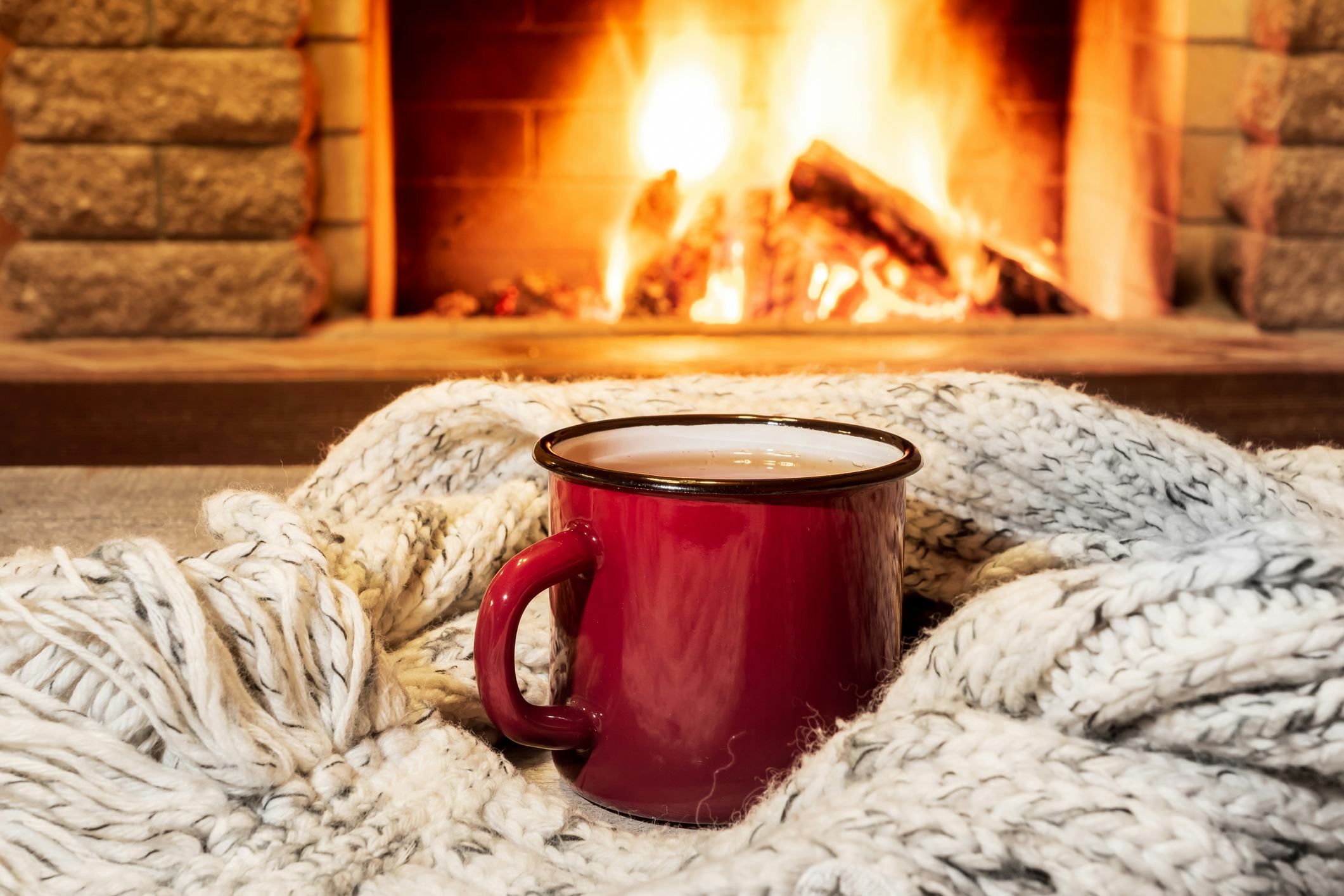 Red enameled mug for hot tea and cozy warm scarf near fireplace