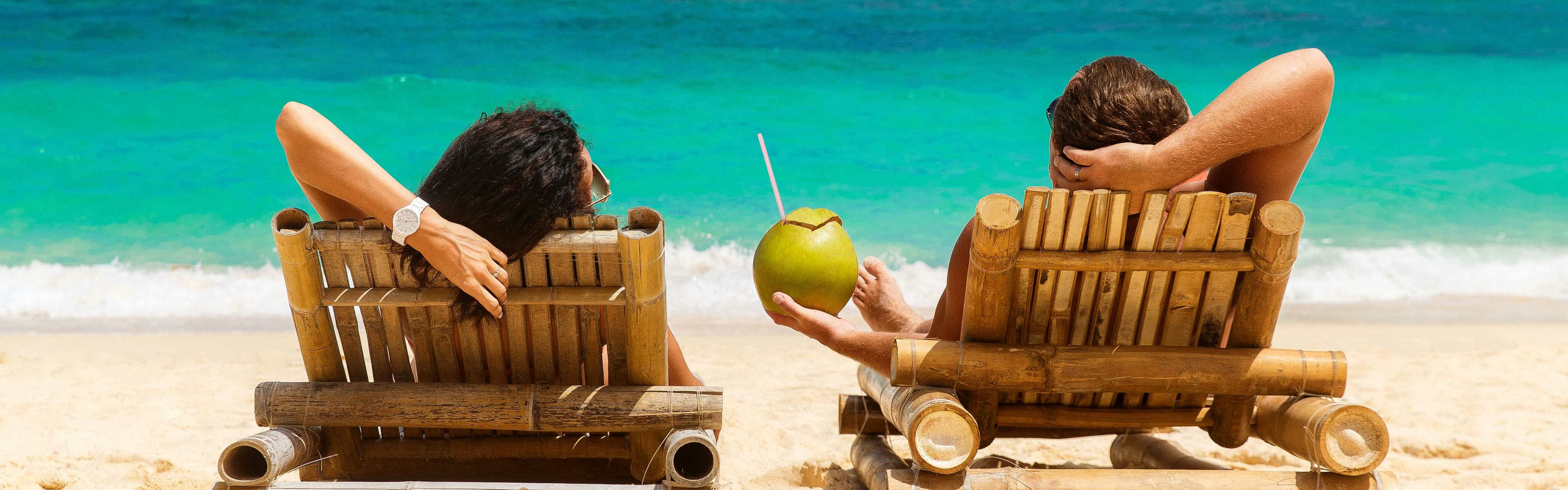 Couple on the beach drinking from a coconut 