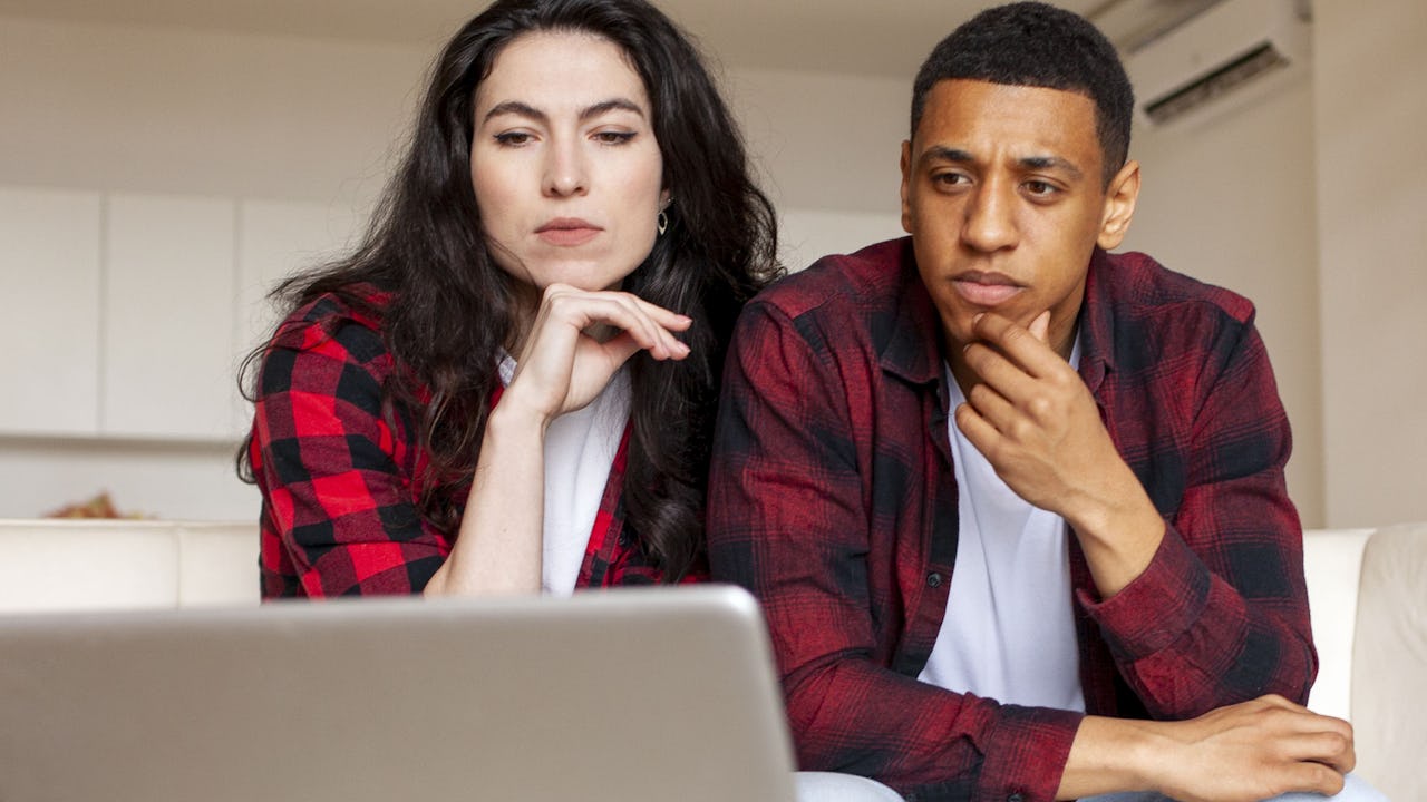 A man and woman thinking over a laptop screen