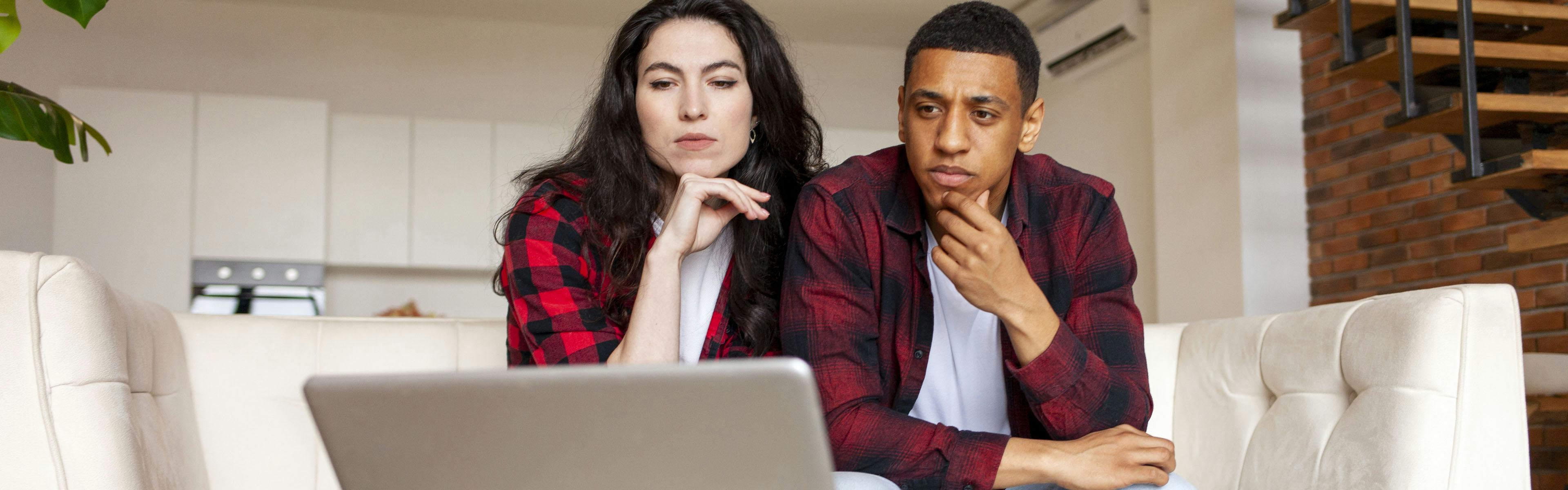 A man and woman thinking over a laptop screen
