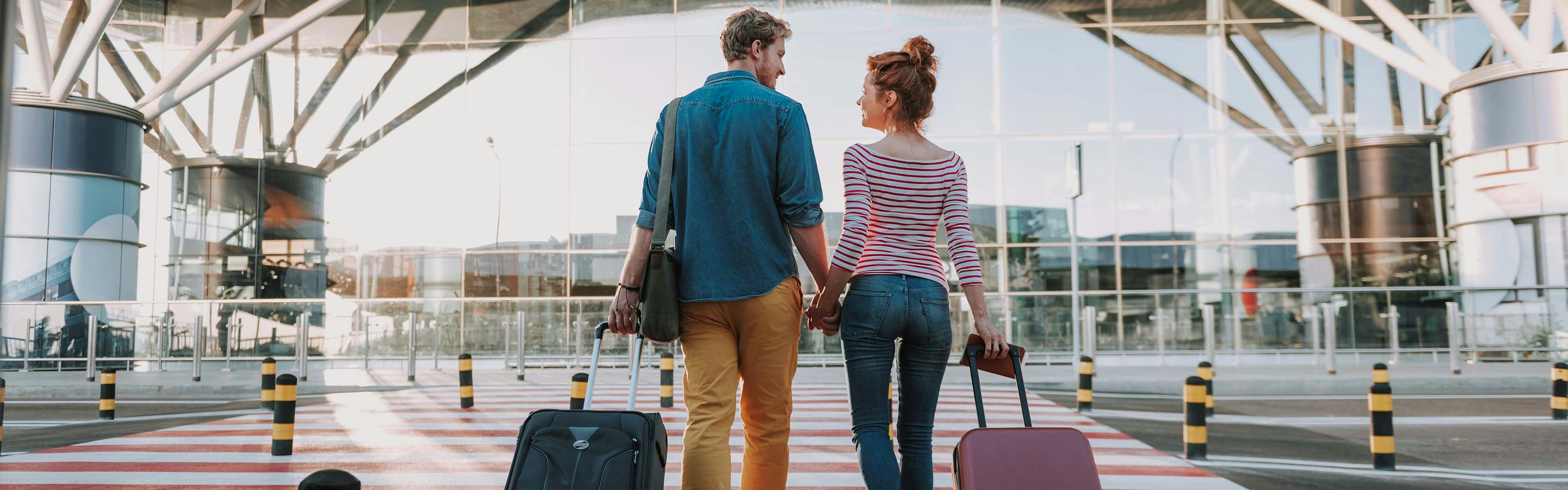 Young Couple walking with suitcases into airport leaving on vacation