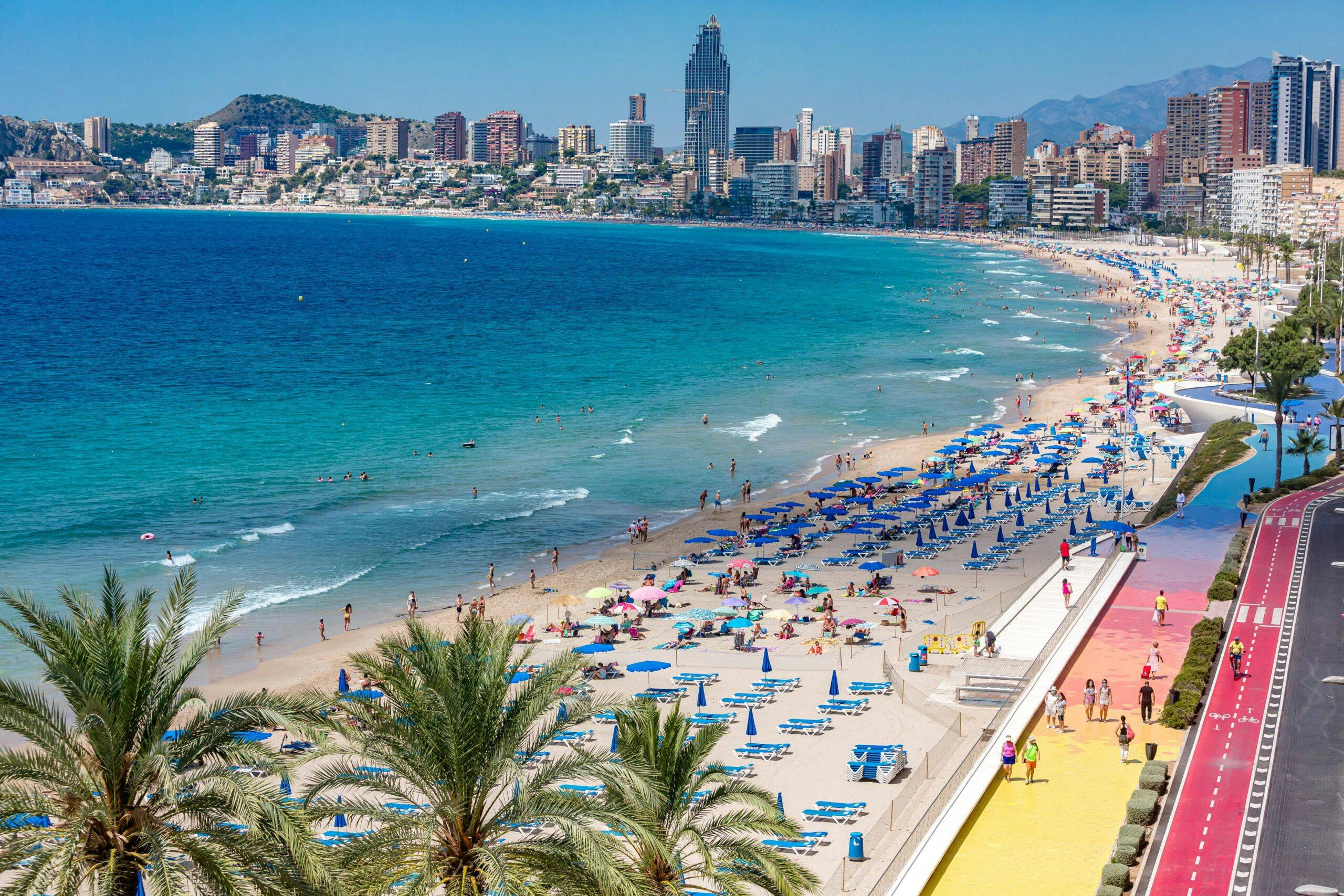 A beautiful beach in Salou with colorful umbrellas and numerous people enjoying the summer sun and sand at Playa de Levante and Playa de Poniente, accessible from Barcelona by the Renfe Regional Express trains.