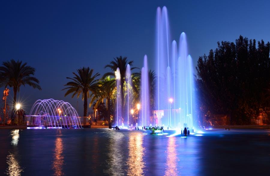 A nighttime view of Fuentes Luminoas in Salou, featuring a fountain illuminated by blue lights, with easy access from Barcelona using the Renfe Regional Express.