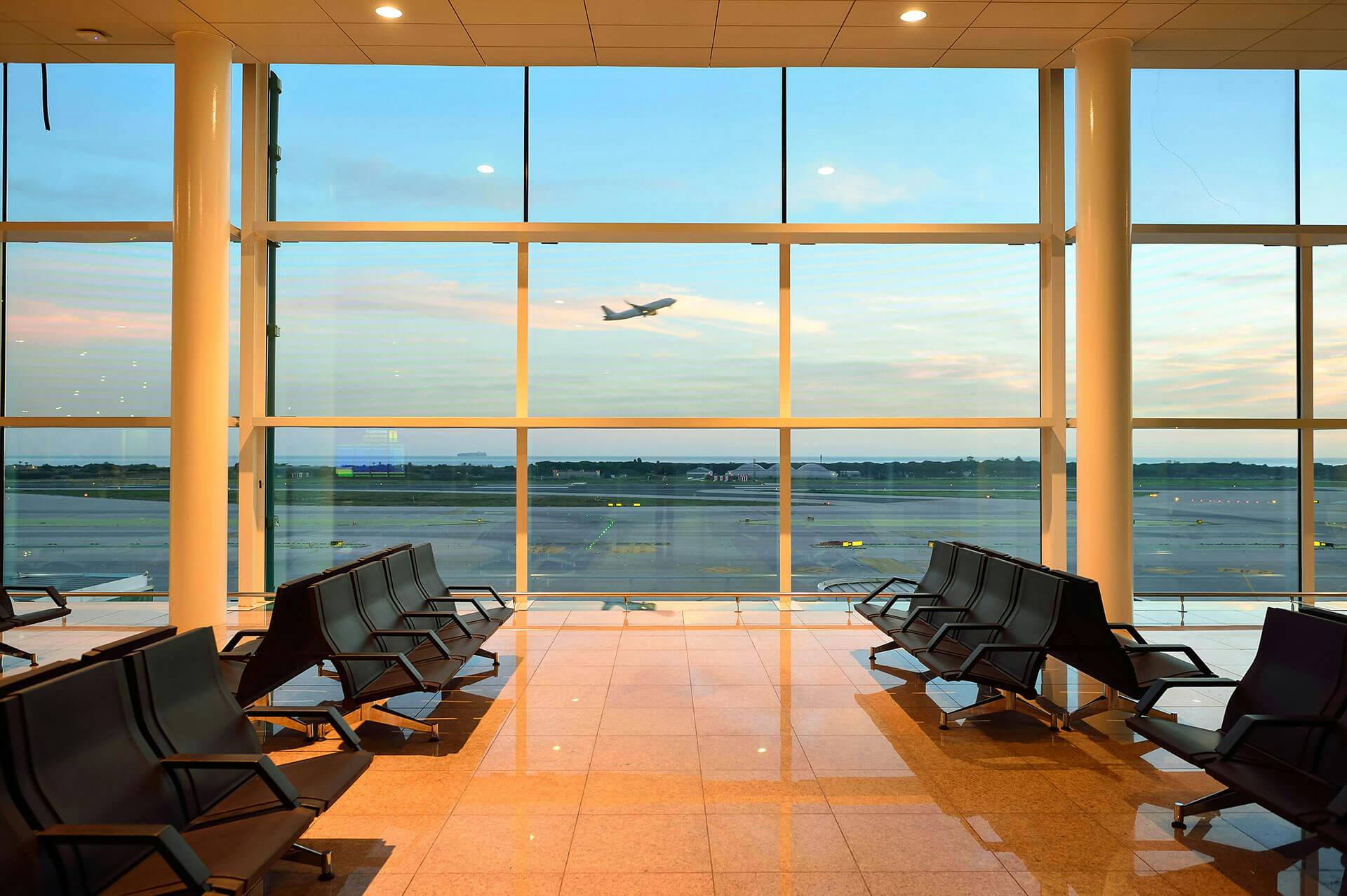 A gate at Barcelona El Prat during sunset, as a plane soars through the sky above.