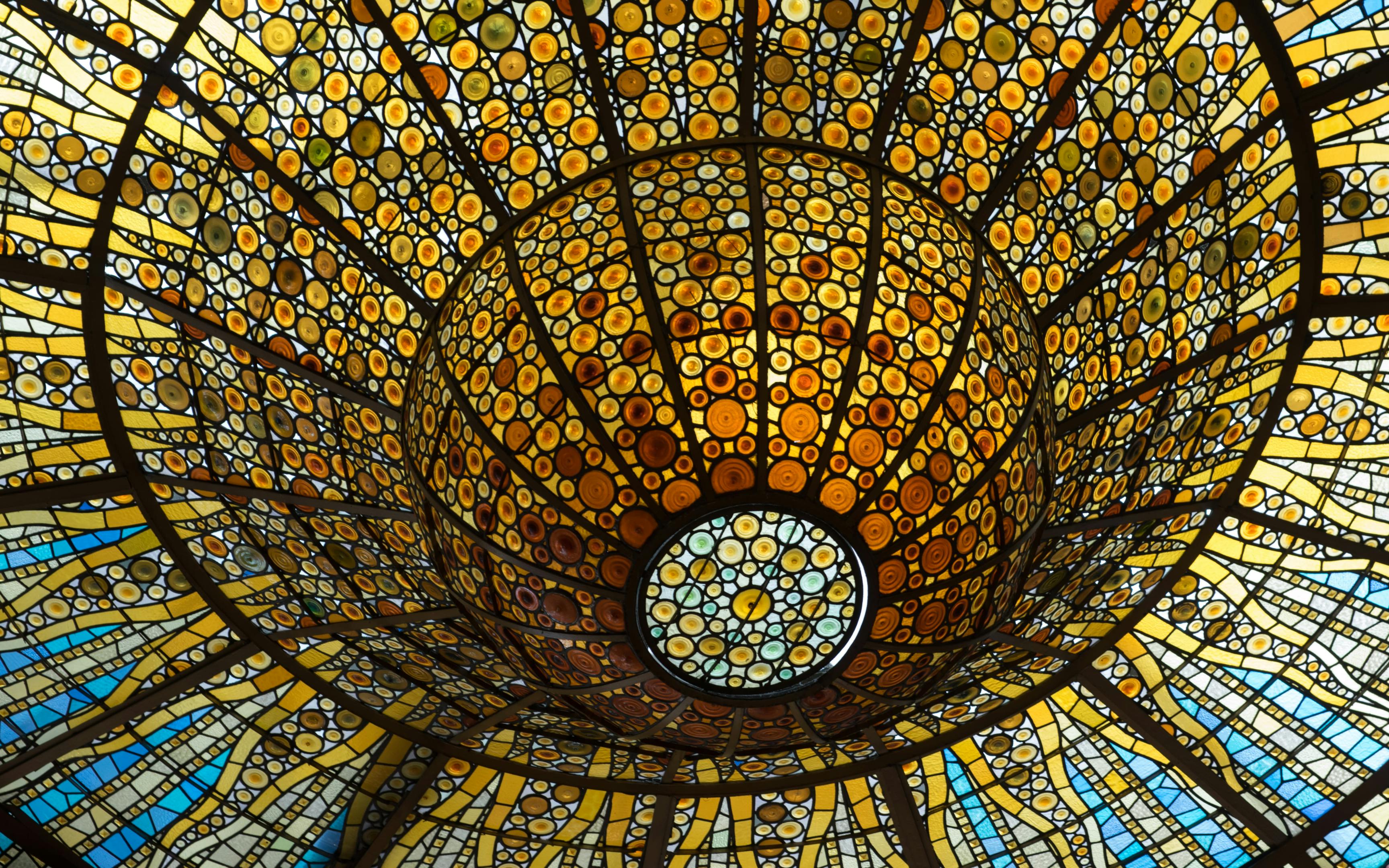 Circular stained glass ceiling at Palau de la Musica Catalana in Barcelona, showcasing intricate design.