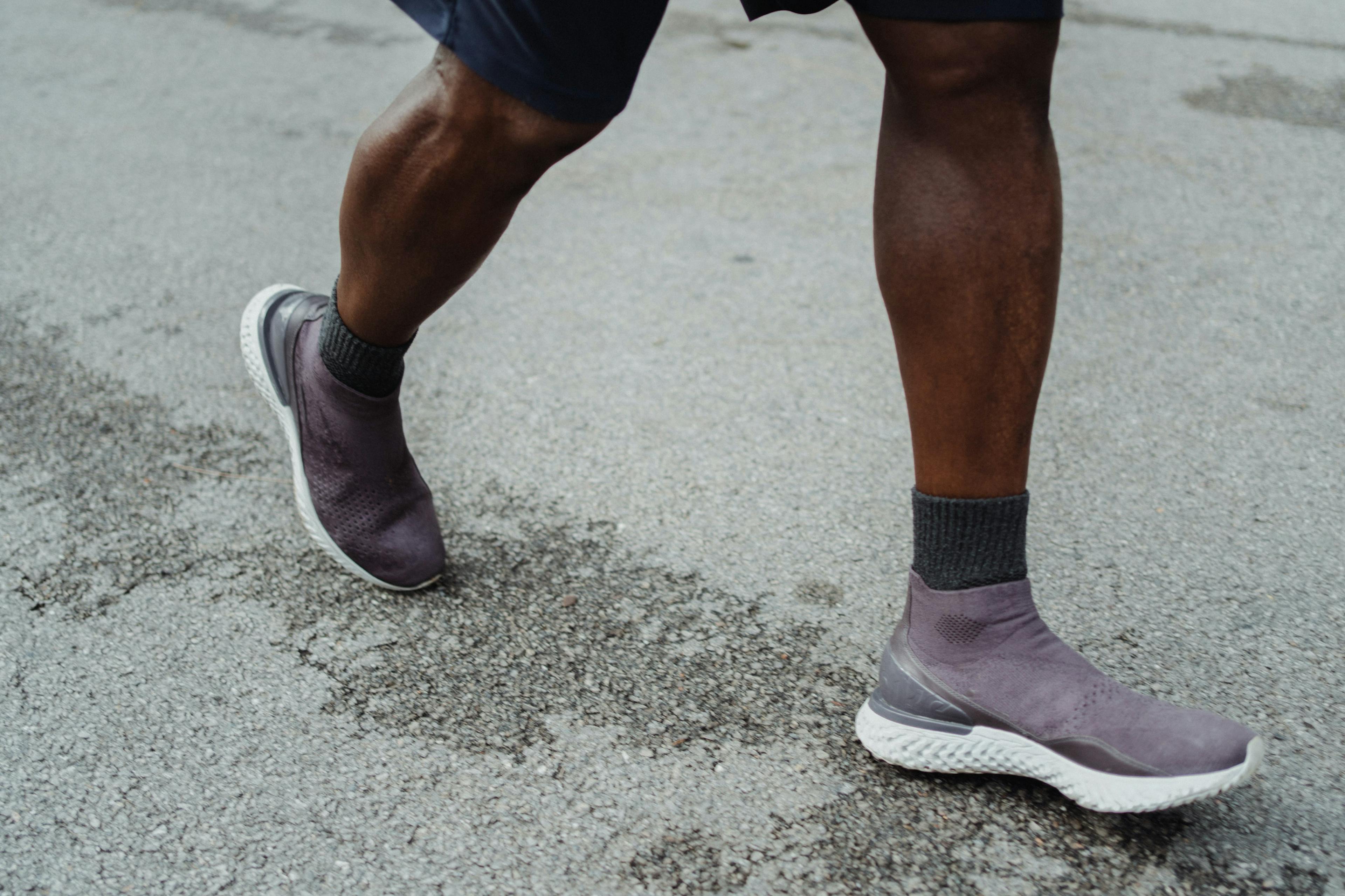 A man in purple sneakers and gray socks walking on the street.