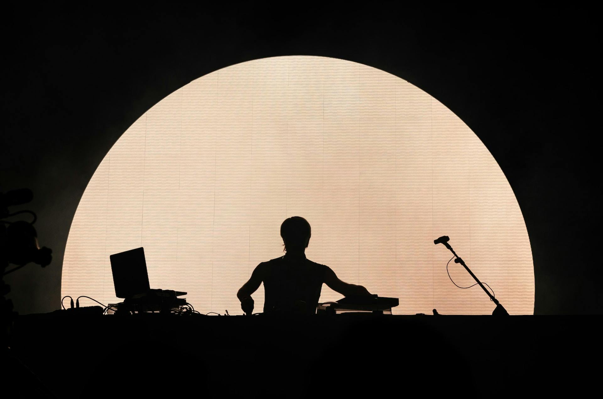 A DJ silhouette stands before a massive circular light at Sonar Festival, where music, creativity, and technology converge.