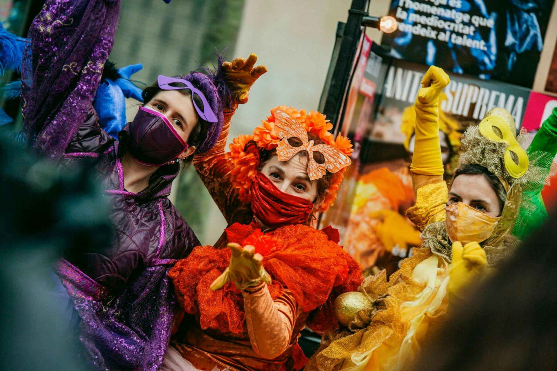 Three people in vibrant costumes and masks, celebrating Carnaval de Barcelona with bright colors.