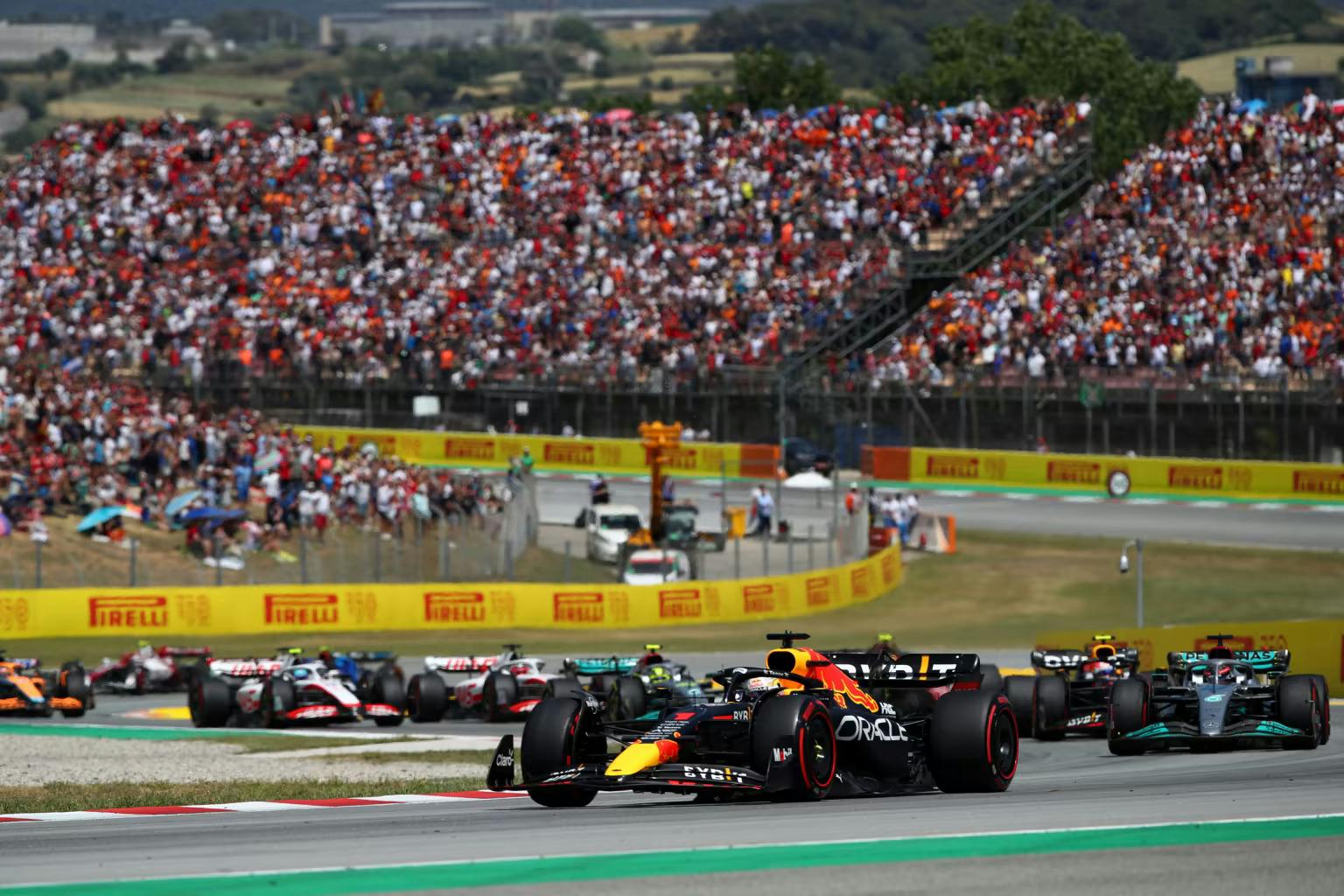 A race car speeds down the track at the Formula One Spanish Grand Prix, with a crowd of spectators watching in anticipation.